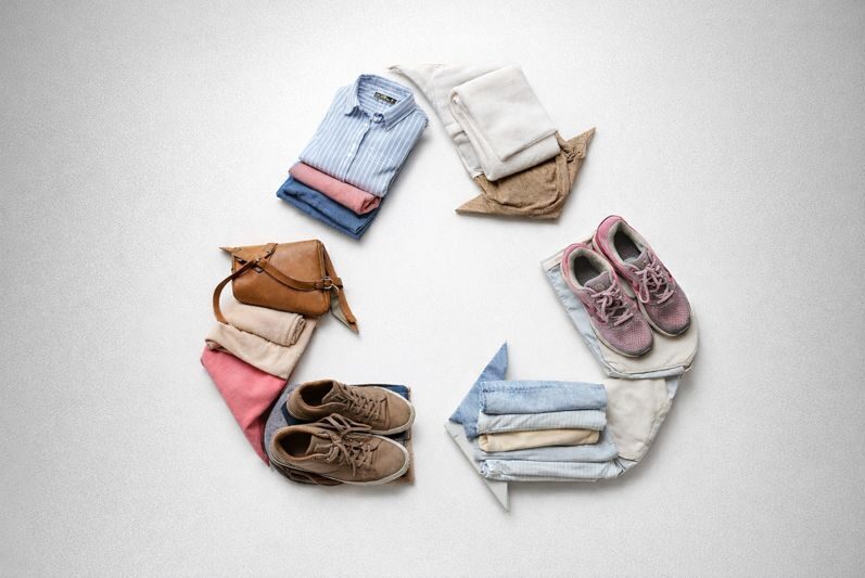 Recycling-Symbol aus Pfeilen, gefüllt mit Kleidungsstücken wie Kleidung, Schuhen, Taschen und weiteren Textilien.